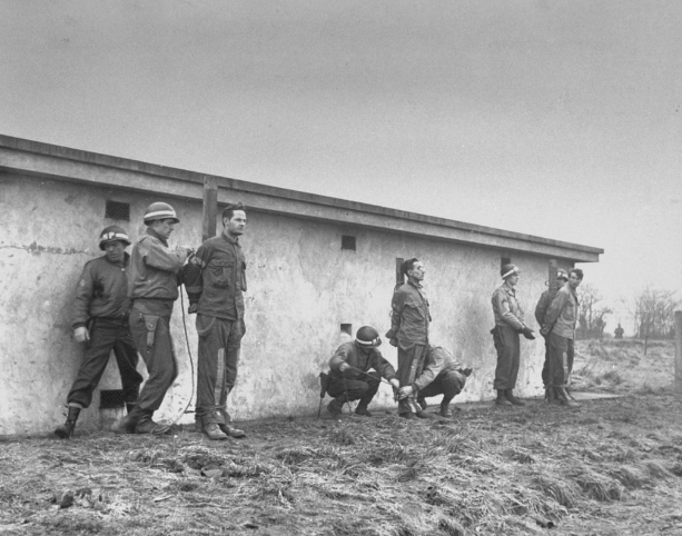 Снято 23 декабря 1944 года и опубликовано в журнале LIFE в июне 1945 года. За тюремным блоком солдаты привязывают немецких заключенных к кольям. Судимых и признанных виновными в шпионаже, они вот-вот будут казнены.